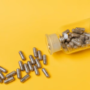 A glass bottle spilling capsules on a vivid yellow background. Perfect for healthcare and medicine themes.